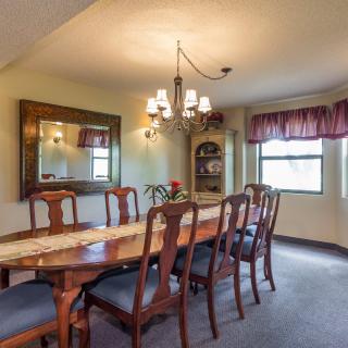 A traditional dining room with a long wooden table and elegant chairs, complemented by a chandelier and mirror.