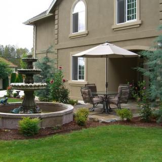 A serene patio with a fountain and outdoor seating in a well-landscaped garden.