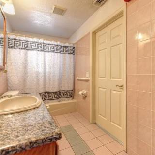 A bathroom featuring a granite countertop, sink, bathtub with a patterned shower curtain, and tiled flooring.