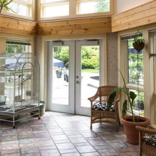 A bright sunroom with French doors, plants, and a cozy chair, filled with natural light.