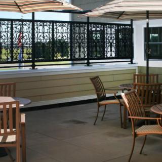 An outdoor patio area with tables, chairs, and umbrellas surrounded by a decorative privacy screen.