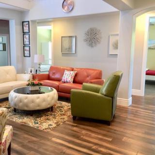 A cozy living room featuring a red couch, green armchair, and tufted coffee table on a decorative rug with hardwood flooring.