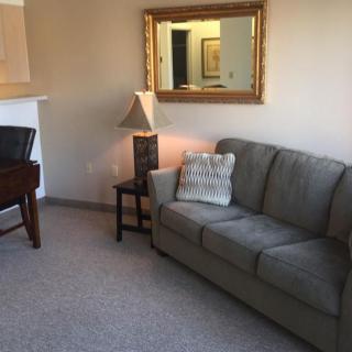 A cozy living room with a sofa, side table, lamp, and a large mirror on the wall.