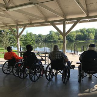 A group of seniors in wheelchairs enjoying the serene view of a lake.