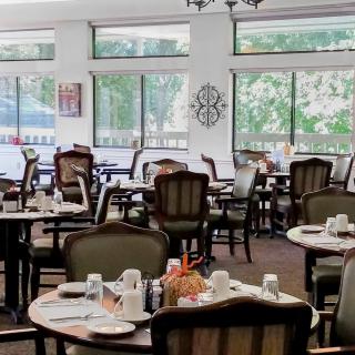 A spacious dining area featuring neatly arranged tables and chairs, set with place settings, surrounded by large windows.
