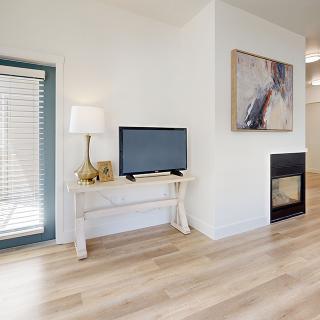A minimalist living room featuring a TV on a white console table, an abstract artwork above a modern fireplace, and light wood flooring.