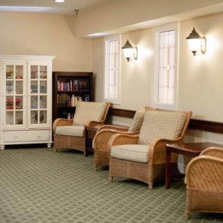 A cozy waiting area with wicker chairs and bookshelves, featuring soft lighting and a carpeted floor.