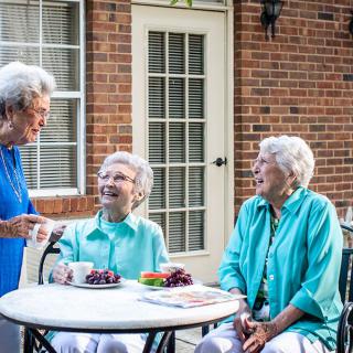A group of elderly women enjoying a conversation outdoors while sitting at a table.