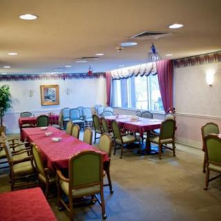 A spacious dining room with red-tableclothed tables, surrounded by cushioned chairs and adorned with large windows and decorative curtains.