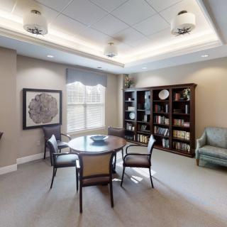 A cozy office space featuring a round table surrounded by chairs, with bookshelves and large windows providing ample natural light.