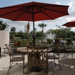A tranquil patio setting with a table and chairs under a red umbrella, overlooking a garden and fountain.