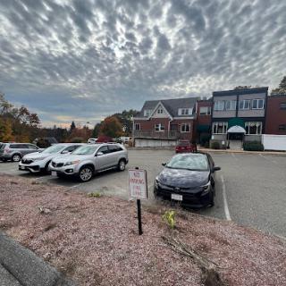 A cloudy day at a parking lot with various cars parked in front of a building.