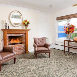 A cozy living room featuring a fireplace, two leather chairs, and floral decorations.