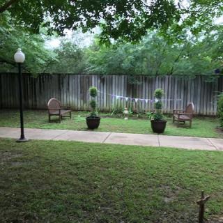 A tranquil garden setting with chairs, neatly trimmed plants, and a lamppost beside a wooden fence.