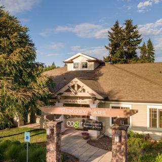 A charming house with a landscaped entrance, surrounded by trees under a blue sky.