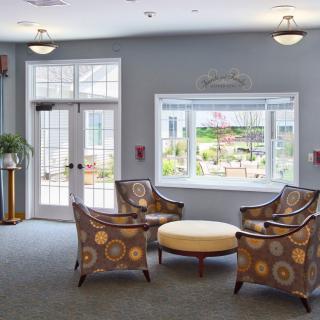 A cozy lobby seating area with patterned chairs and a round table, illuminated by natural light from a large window.