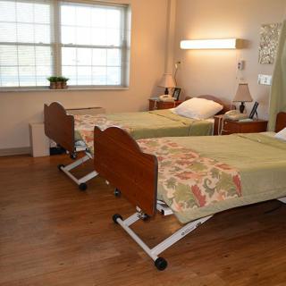A clean and organized hospital room with two beds, featuring a well-lit space and wood flooring.