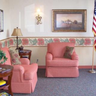 A cozy living room with pink armchairs, a lamp, artwork on the wall, and an American flag in the corner.