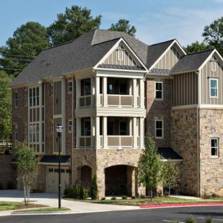 A modern multi-story house with stone exterior and balconies set amidst trees.