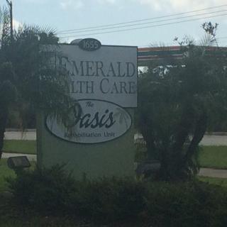 A sign for Emerald Health Care Oasis surrounded by greenery.