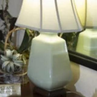 A ceramic table lamp with a white lampshade, placed on a wooden table beside a mirror.