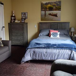A cozy bedroom with a bed, dresser, and wall art.