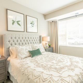 A bright and modern bedroom featuring a tufted headboard, decorative pillows, and minimalist artwork above the bed.