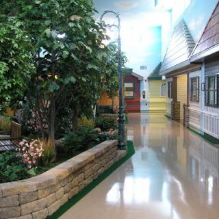 A serene indoor space resembling a garden with a pathway surrounded by decorative houses and lush greenery.