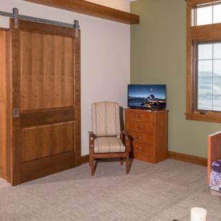 An office space with a wooden chair, a TV on a cabinet, and a sliding wooden door.