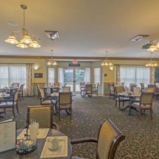 A spacious dining room with neatly arranged tables and chairs, illuminated by elegant lighting fixtures.