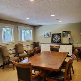 A spacious meeting room featuring a large wooden table surrounded by chairs, with natural light coming from the windows and a dartboard on the wall.