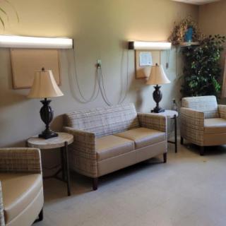 A comfortable waiting room with wicker couches and armchairs, accompanied by lamps and indoor plants.