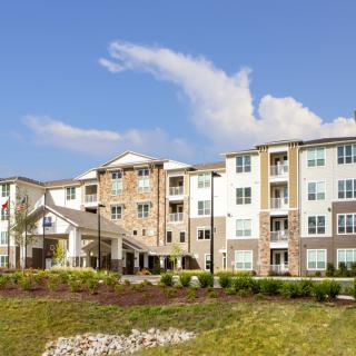 A modern apartment building with landscaped surroundings under a blue sky.