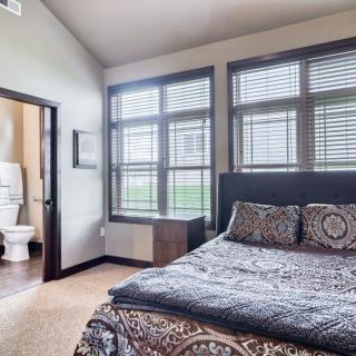 A cozy bedroom with large windows, featuring a comfortable bed and an adjoining bathroom.