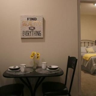 A cozy dining area with a small table set for two, featuring wall art and a glimpse into a bedroom.