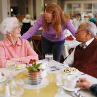 A group of seniors enjoying a meal and conversation in a communal dining setting.