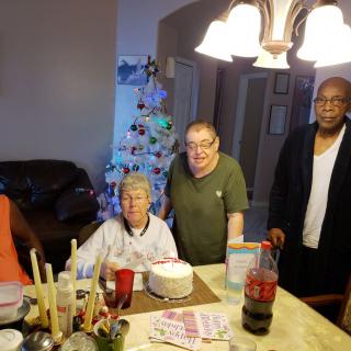 Family gathering around a table with a cake, celebrating indoors.