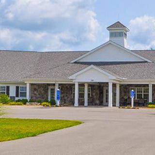 A large residential building with a covered entrance and a spacious parking area on a cloudy day.