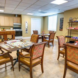 A cozy community room featuring multiple tables set up with board games, comfortable seating, and a small kitchen area.