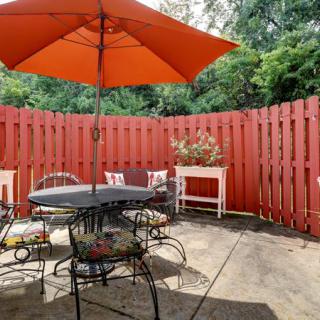A cozy outdoor patio space with a red fence, featuring a table and chairs under an orange umbrella.