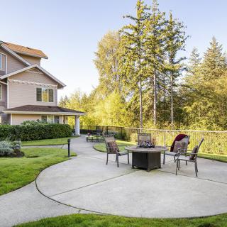 A serene backyard patio with chairs and a fire pit surrounded by greenery.