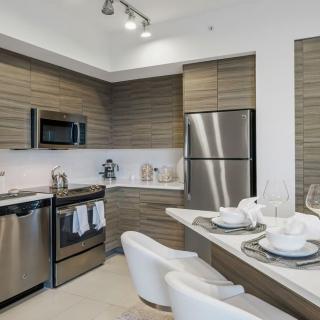 A modern kitchen featuring stainless steel appliances and wood cabinetry with a cozy bar seating area.