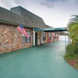 A building with a stone wall exterior, an American flag, and a green canopy over the entrance, surrounded by outdoor greenery.