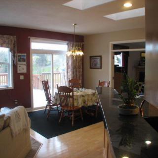 A cozy kitchen and dining area with a wooden table and chairs, featuring natural light from large windows.