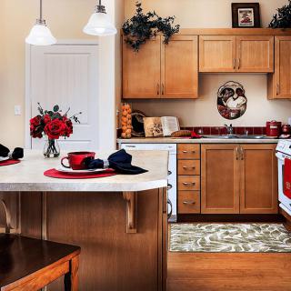 A cozy kitchen with wooden cabinets, featuring red accents and a central island adorned with flowers.