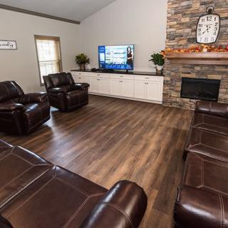 A cozy living room with leather seating, a large TV, and a stone fireplace.