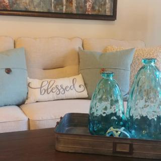 A cozy living room setup featuring a beige sofa with decorative pillows and a wooden coffee table adorned with blue glass vases.