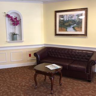 A cozy corner in a living room featuring a brown leather sofa, a small table with magazines, and decorative artwork on the walls.