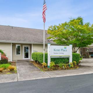A one-story building with an American flag and a sign reading 'Forest Place Apartments' near the entrance, surrounded by well-maintained landscaping.