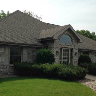A stone-faced residential house with well-maintained landscaping and a peaked roof.